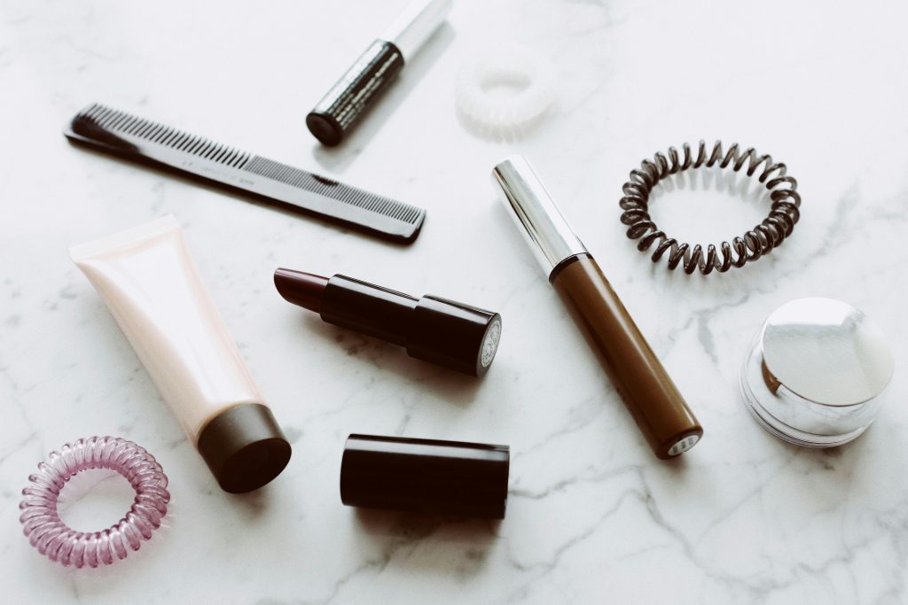A flat lay of various cosmetics and hair accessories on a marble surface.